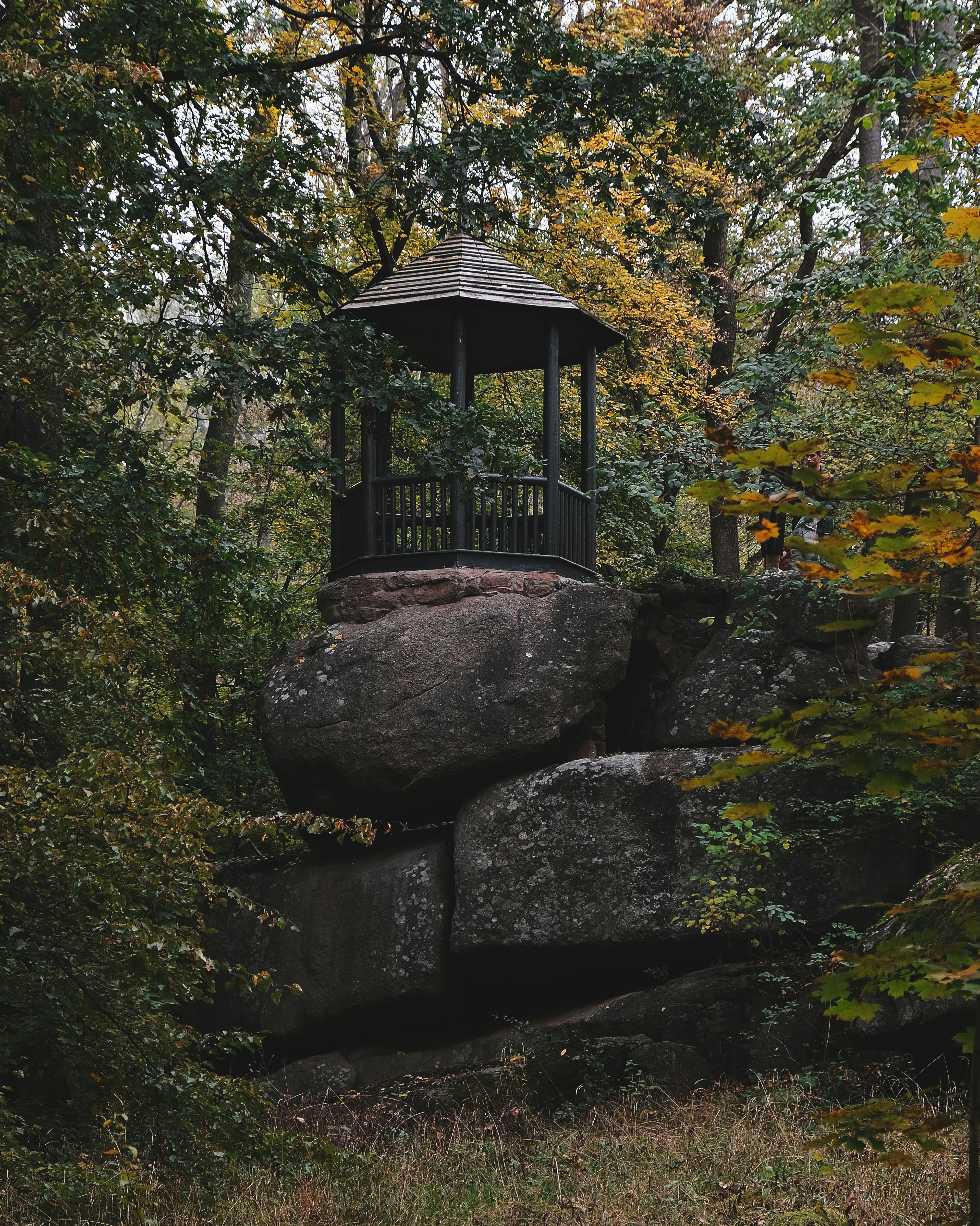 brown wooden gazebo on gray rock formation surrounded by green trees during daytime